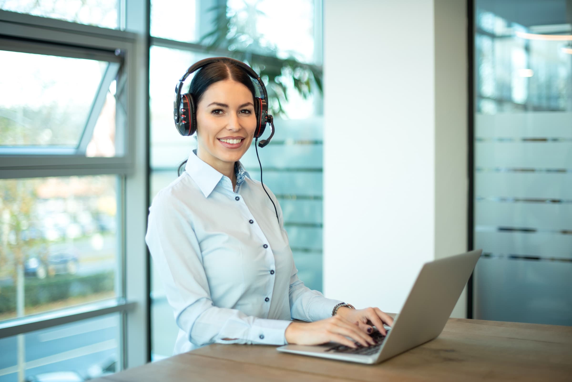A friendly customer-support agent on a headset, smiling during a call in a modern office.